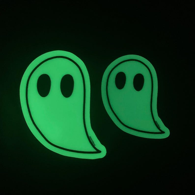 A simple, minimal illustration of a ghost with two black eyes and a black outline. The body of the ghost is white and glows in the dark in green. Two ghosts are shown here to show the two different sizes available