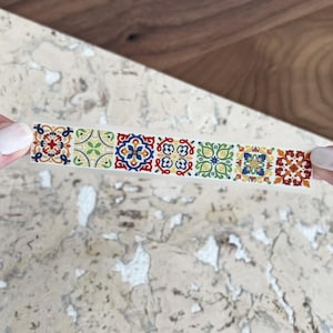 Puede incluir: Un rollo de cinta washi decorativa con un patrón repetitivo de azulejos geométricos coloridos. La cinta es blanca con un fino borde negro.