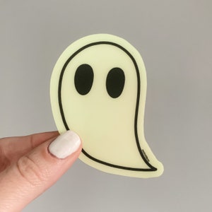 May include: A yellow glow-in-the-dark ghost sticker with black eyes. The sticker has a simple design and is perfect for adding a spooky touch to any surface.
