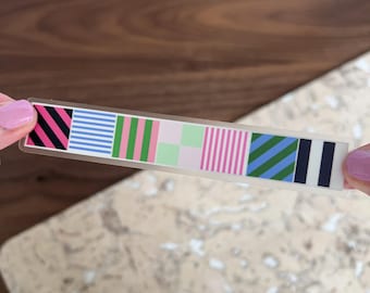 May include: A clear sticker sheet with eight different patterned strips. The patterns include black and white stripes, blue and white stripes, green and pink stripes, pink and white stripes, green and blue stripes, and black and white stripes.