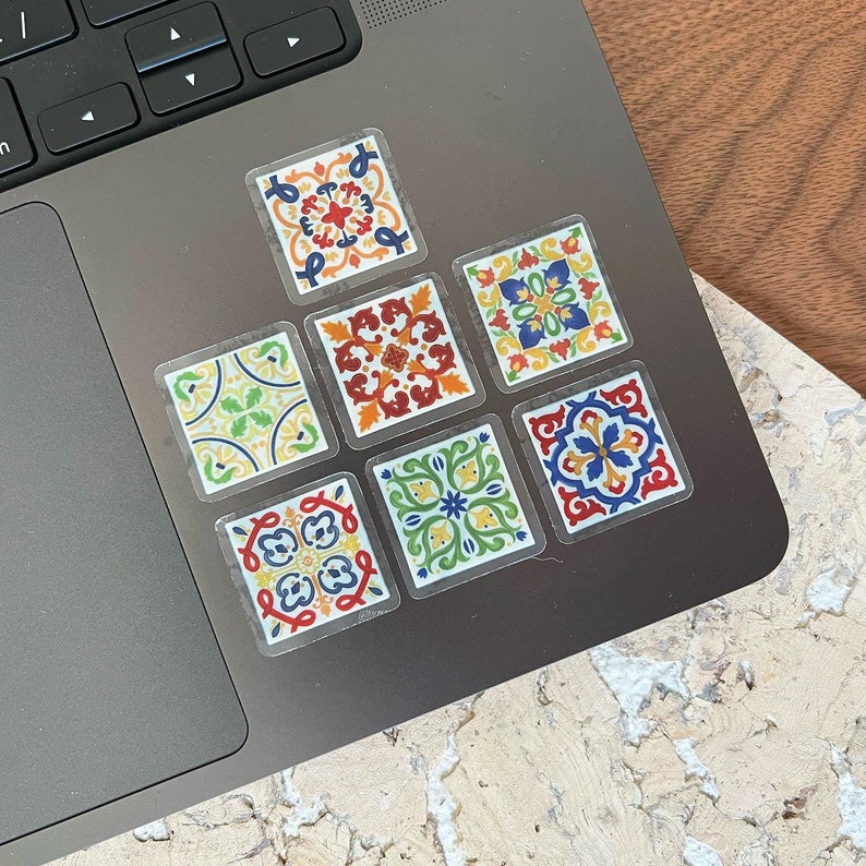 K&ouml;nnte beinhalten: Ein Satz von acht bunten Fliesenaufklebern mit geometrischen Mustern. Die Aufkleber sind in einem Rastermuster auf einem Laptop angeordnet.