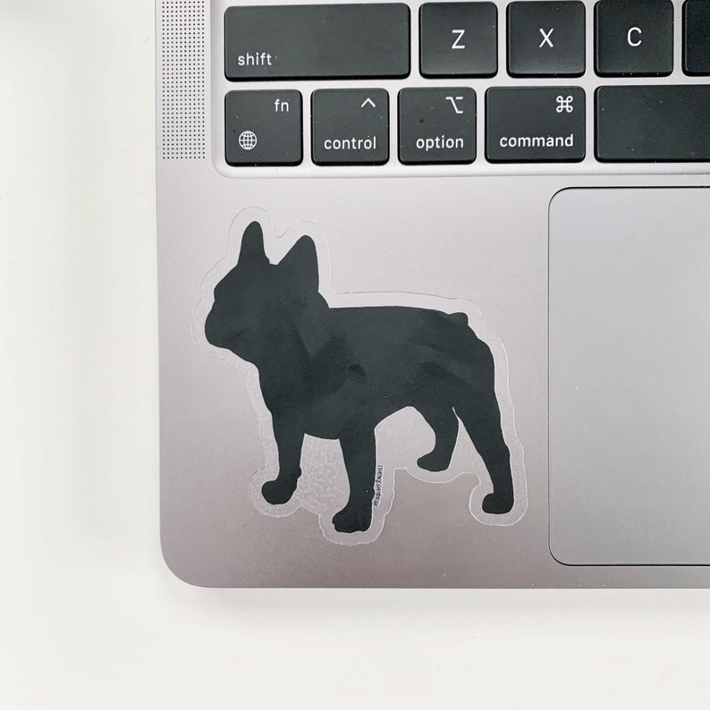 May include: A black sticker featuring a silhouette of a French Bulldog. The sticker is placed on a laptop, with the keyboard visible. The dog is in a standing position, with its ears perked up.