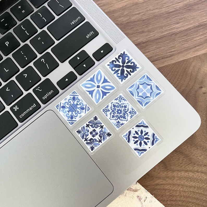May include: A set of six blue and white patterned tile stickers. The stickers are arranged in a grid pattern on a silver laptop.