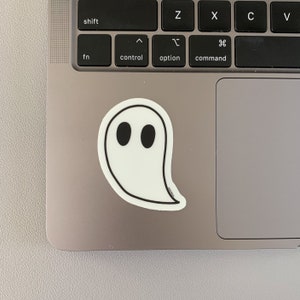 May include: A white ghost sticker with black eyes on a silver laptop.
