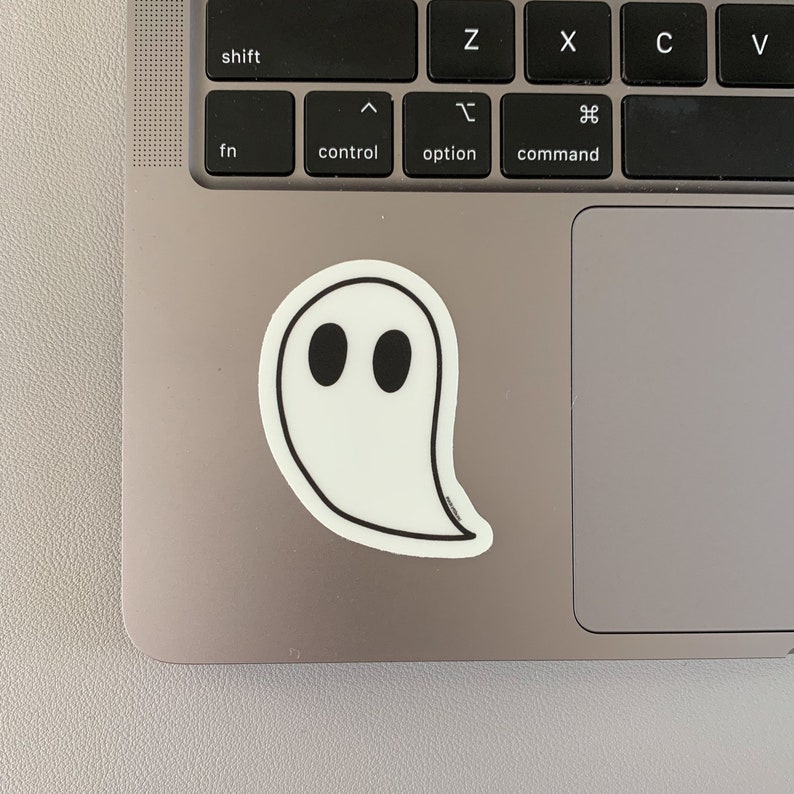 May include: A white ghost sticker with black eyes on a silver laptop.