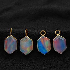 May include: Four hexagonal pendants with iridescent, multicolored centers and gold-colored metal frames. Each pendant has a small loop at the top for hanging. The pendants are displayed on a black background.