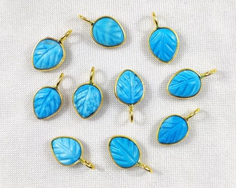 May include: Ten turquoise blue leaf-shaped pendants with gold-toned accents. Each pendant features a carved leaf design.