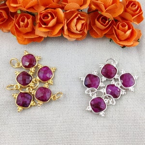 May include: Two sets of five purple gemstone charms with gold and silver settings. The charms are in the shape of a square with rounded corners. The charms are arranged in a cluster.