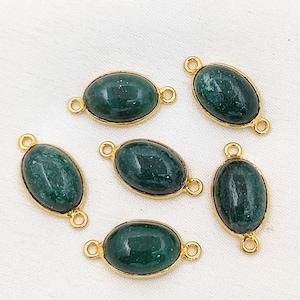 Pode incluir: Seis conectores ovais de pedras preciosas verdes com biséis e laços dourados. As pedras preciosas têm uma aparência manchada. Estes conectores são adequados para a fabricação de joias, como pulseiras ou colares.