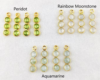May include: Three sets of three gemstone charms, each set hanging from a gold loop. The charms are green peridot, white rainbow moonstone, and light blue aquamarine. The text "Peridot", "Rainbow Moonstone", and "Aquamarine" is printed below each set.