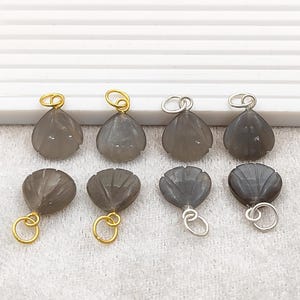 May include: Eight gray gemstone pendants with carved petal designs. The pendants have gold and silver-colored loops for attaching to jewelry. The gemstones are teardrop-shaped and have a polished finish.