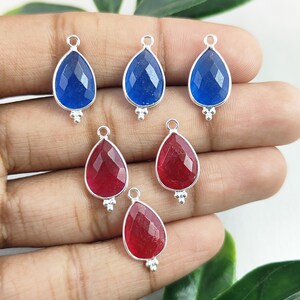 May include: Five silver teardrop-shaped pendants with faceted gemstone inserts. Two pendants have blue gemstones and three pendants have red gemstones.