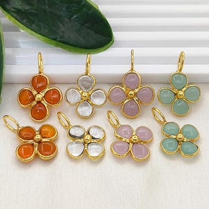 Puede incluir: Una colección de colgantes dorados en forma de trébol con incrustaciones de piedras de varios colores. Los colores incluyen naranja, transparente, rosa y verde. Cada colgante tiene un pequeño lazo para colgar.