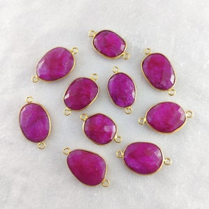 May include: Ten pink gemstone connector charms with gold-toned metal accents. Each charm features a faceted oval-shaped gemstone with two loops on either side.