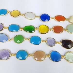 May include: Close-up of several strands of colorful gemstone jewelry. Each strand features irregularly shaped, faceted gemstones in various colors, including blue, green, yellow, and orange, set in gold-colored metal. The gemstones are linked together to form a necklace or bracelet.