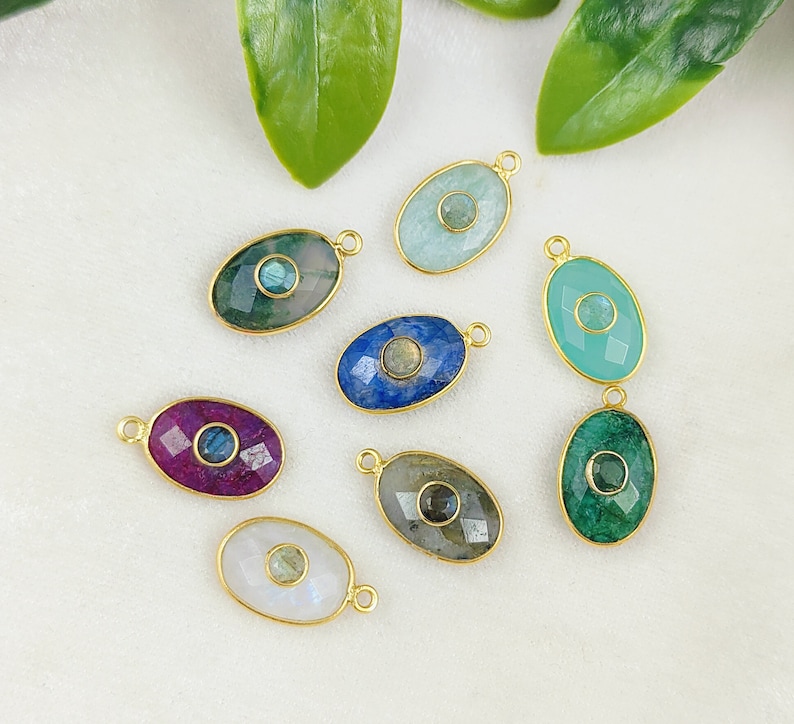 May include: Eight oval-shaped gemstone pendants with gold-toned accents. Each pendant features a different gemstone, including blue, green, pink, and white.