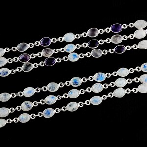 May include: A silver chain necklace with oval-shaped moonstone and amethyst gemstones. The necklace is layered with multiple strands.