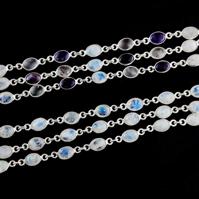 May include: A silver chain necklace with oval-shaped moonstone and amethyst gemstones. The necklace is layered with multiple strands.