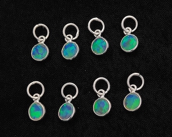 May include: Eight small, round opal charms with silver-colored loops. The opals display a mix of blue and green colors. The charms are set against a black background.