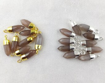 Puede incluir: Dos juegos de colgantes de piedra preciosa con detalles dorados y plateados. Los colgantes son de color marrón claro y tienen una forma puntiaguda.