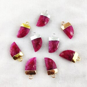 May include: Ten pink gemstone pendants with gold and silver accents. The pendants are shaped like a crescent moon and have a faceted finish.