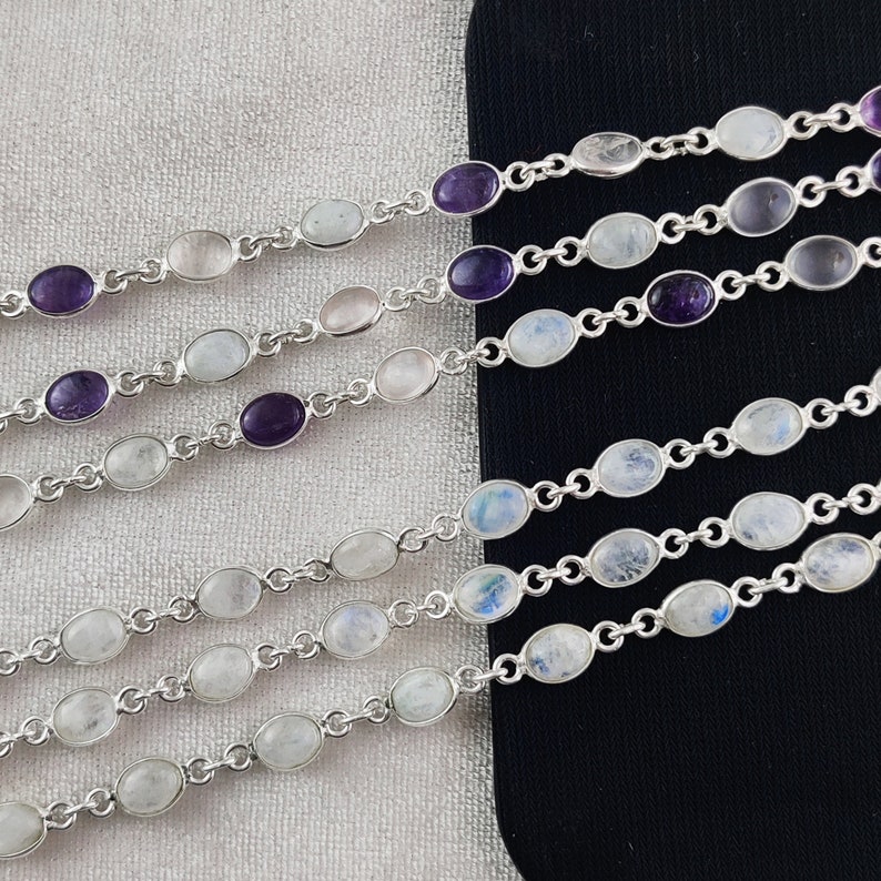 May include: Five silver bracelets with oval-shaped moonstone and amethyst gemstones. The bracelets are layered on a black surface.