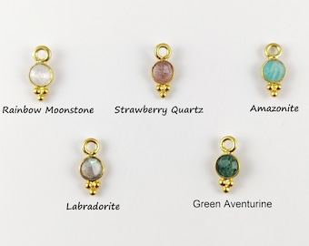 May include: Five gold-colored gemstone charms with different stones: rainbow moonstone, strawberry quartz, amazonite, labradorite, and green aventurine. Each charm has a loop at the top and three small decorative beads at the bottom. The names of the stones are written below each charm.