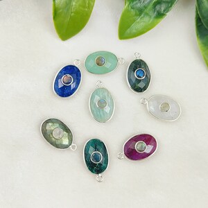 May include: Assortment of oval-shaped gemstone pendants with silver settings. Each pendant features a different gemstone, including blue, green, white, and pink.