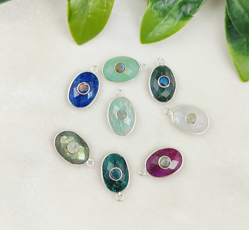 May include: Assortment of oval-shaped gemstone pendants with silver settings. Each pendant features a different gemstone, including blue, green, white, and pink.