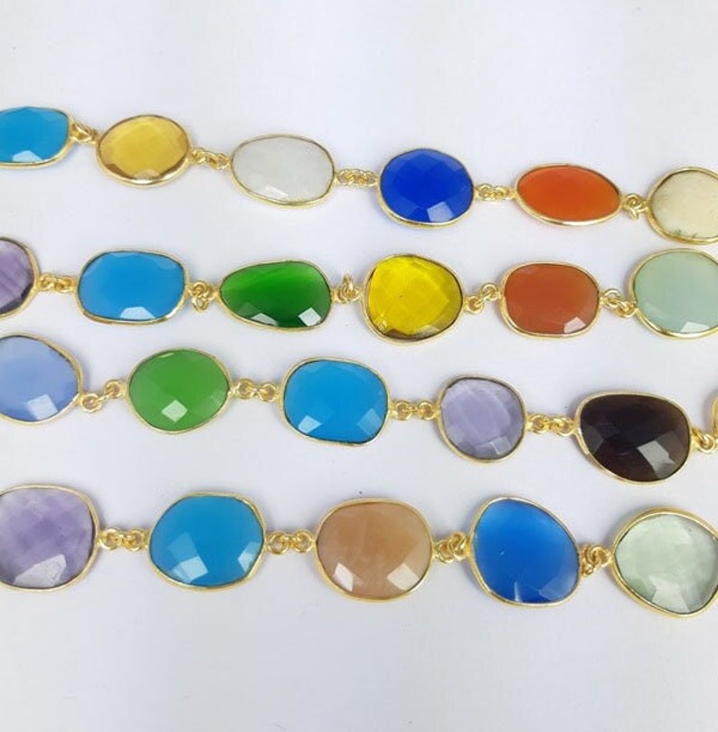 May include: Close-up of several strands of colorful gemstone jewelry. Each strand features irregularly shaped, faceted gemstones in various colors, including blue, green, yellow, and orange, set in gold-colored metal. The gemstones are linked together to form a necklace or bracelet.