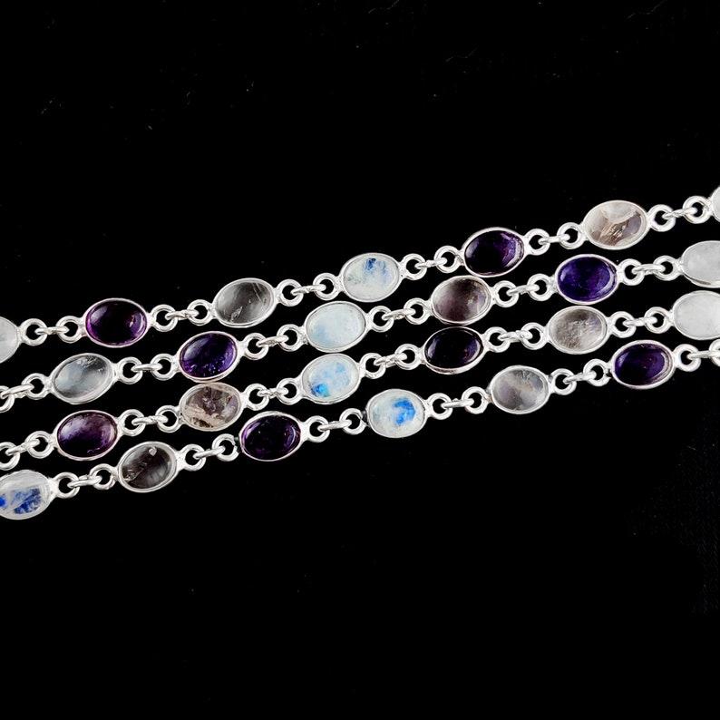 May include: A silver chain bracelet with oval-shaped gemstones in shades of purple, white, and gray.