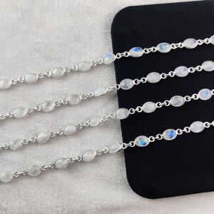 May include: Five silver bracelets with oval-shaped moonstone beads. The bracelets are arranged in a row on a black surface.