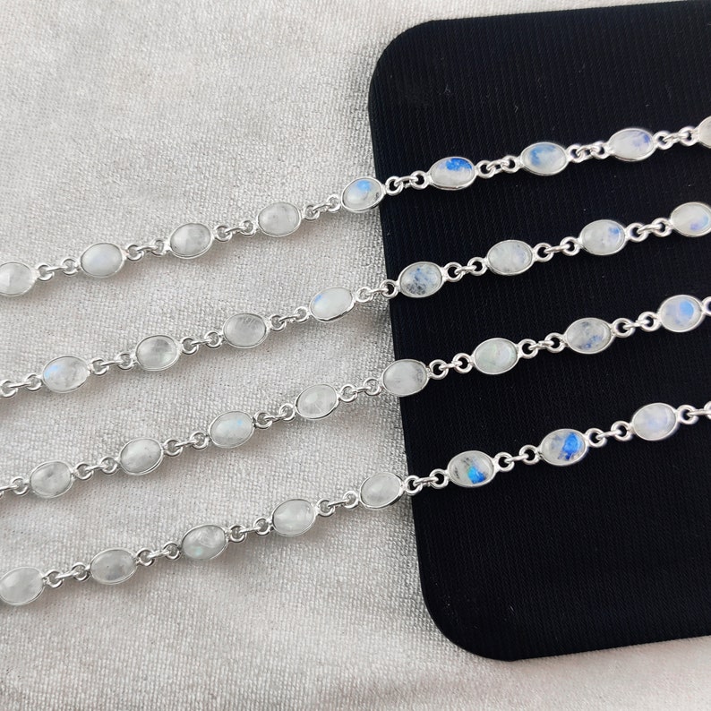 May include: Five silver bracelets with oval-shaped moonstone beads. The bracelets are arranged in a row on a black surface.