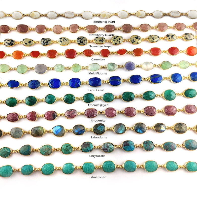 May include: A close-up of ten rows of gemstone bracelets with gold chain links. Each row features a different gemstone, including mother of pearl, strawberry quartz, dalmatian jasper, carnelian, multi fluorite, lapis lazuli, emerald, rhodonite, labradorite, chrysocolla, and amazonite.