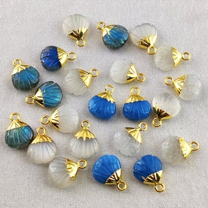 Peut inclure: Assortiment de 18 pendentifs en forme de coquille plaqués or avec différentes incrustations de pierres précieuses. Les pierres précieuses comprennent le labradorite bleu, la pierre de lune blanche et la calcédoine bleue.