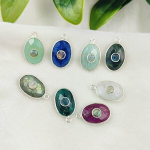May include: Eight silver oval-shaped pendants with different colored gemstones and a smaller gemstone in the center. The gemstones are green, blue, white, and pink.
