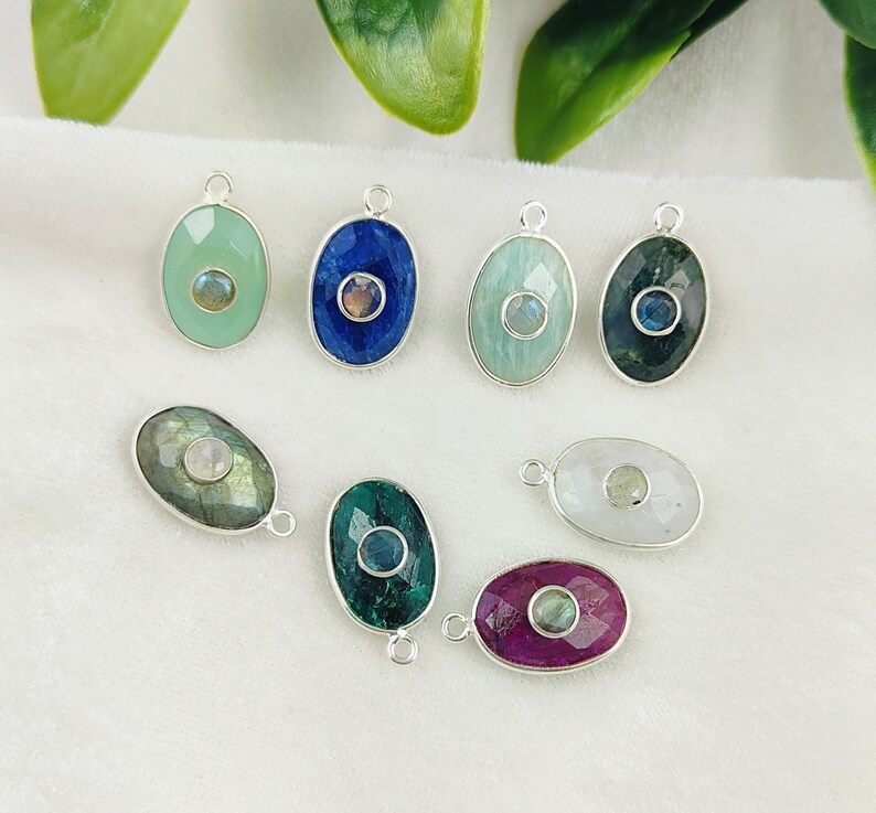May include: Eight silver oval-shaped pendants with different colored gemstones and a smaller gemstone in the center. The gemstones are green, blue, white, and pink.