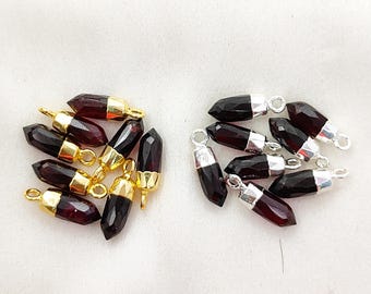 Puede incluir: Una colección de colgantes de piedras preciosas facetadas, de color rojo oscuro y forma puntiaguda. Un grupo presenta tapas de metal dorado con anillas, mientras que el otro grupo tiene tapas de metal plateado con anillas para joyería.