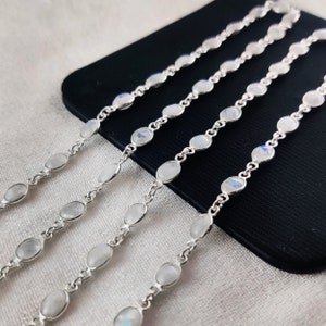 May include: Four silver chains with oval-shaped moonstone beads. The chains are laid out on a black surface.