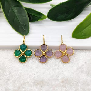 Può includere: Tre paia di orecchini a forma di quadrifoglio color oro. Un paio presenta pietre preziose verdi, un altro ha pietre preziose viola e il terzo ha pietre preziose rosa. Ogni orecchino ha un perno color oro.