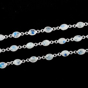 May include: A silver chain necklace with oval-shaped moonstone beads. The beads have a white and blue iridescent shimmer.