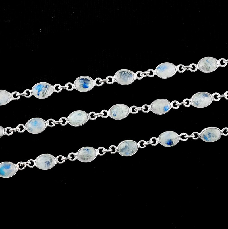 May include: A silver chain necklace with oval-shaped moonstone beads. The beads have a white and blue iridescent shimmer.