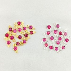 Op de afbeelding: Twee sets robijn-bedels met gouden en zilveren instellingen. De bedels zijn rond en hebben een kleine lus aan de bovenkant om aan sieraden te bevestigen.