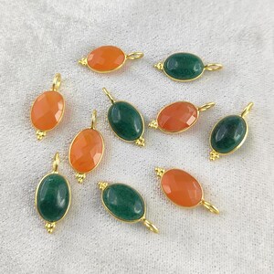 Può includere: Assortimento di ciondoli ovali in pietra preziosa con accenti dorati. I ciondoli sono in tonalità di verde e arancio.