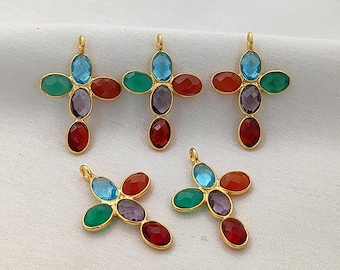 Puede incluir: Colgantes de cruz dorados con piedras preciosas de colores. Cada cruz presenta una combinación de piedras azules, verdes, rojas y moradas. Los colgantes están diseñados con un lazo en la parte superior para sujetarlos.