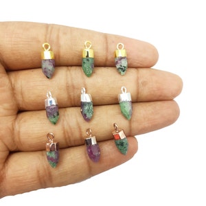 Może przedstawiać: Dziewięć zielonych, różowych i fioletowych zawieszek z kamieni szlachetnych ze złotymi i srebrnymi akcentami. Zawieszki mają kształt łzy i zakończone są spiczastym końcem.