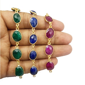 May include: Three gold chain bracelets with oval-shaped gemstones. The bracelets feature green, blue, and red gemstones.
