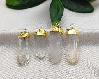 May include: Four clear quartz crystal pendants with gold-colored metal caps and loops for hanging. The crystals vary slightly in size and shape, showcasing natural variations. The pendants are displayed against a light background.