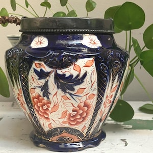 May include: A blue and white ceramic jar with a metal lid. The jar features a floral design in orange and white, with gold accents. The jar is a decorative piece, likely for storage or display.