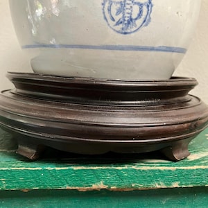May include: A white and blue ceramic bowl with a decorative design, resting on a dark brown wooden stand. The stand has a curved design and three small feet. The bowl has a blue painted design.